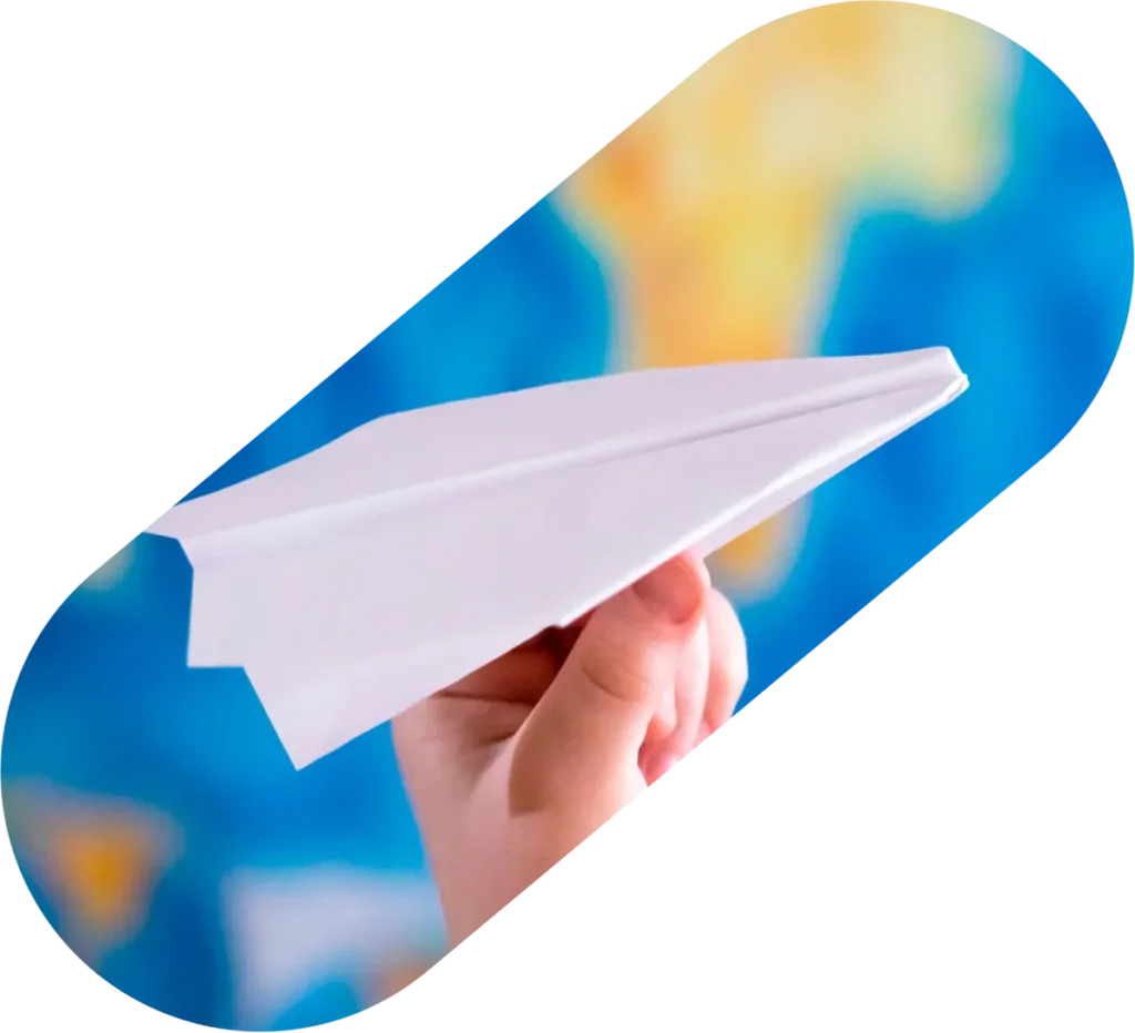 Paper airplane held in front of a colorful world map, symbolizing global travel and connection.